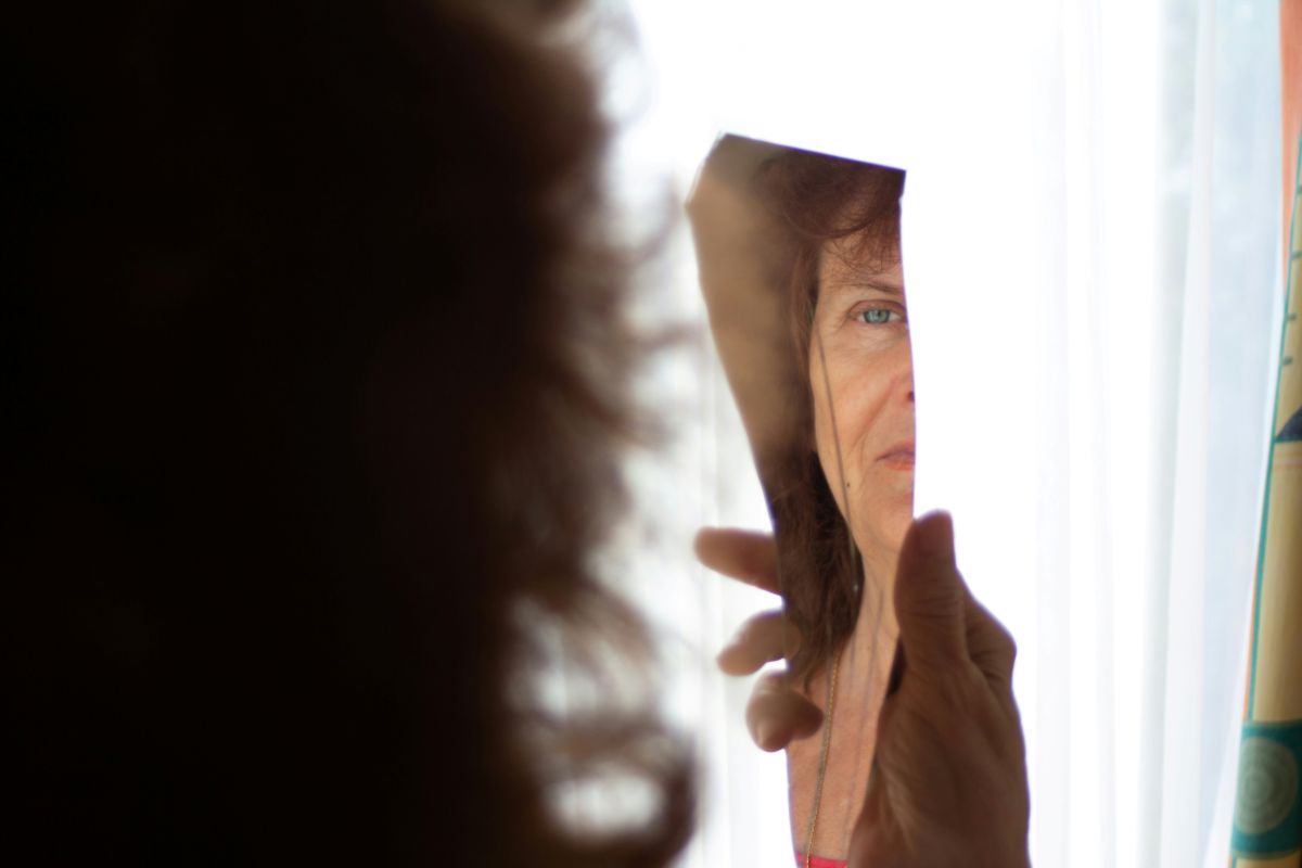 Vrouw kijkt naar haar spiegelbeeld in een gebroken spiegel