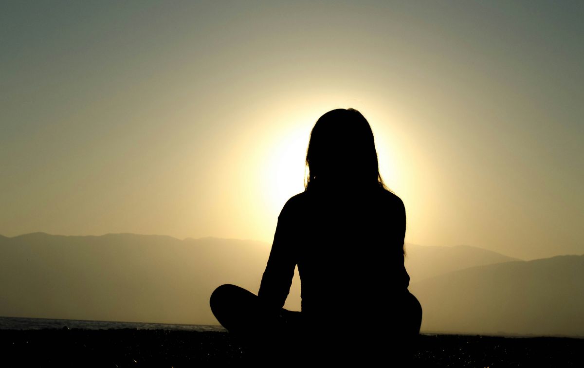 Silhouette of a person sitting quietly at sunrise, reflecting on health, mindful living, and gratitude.