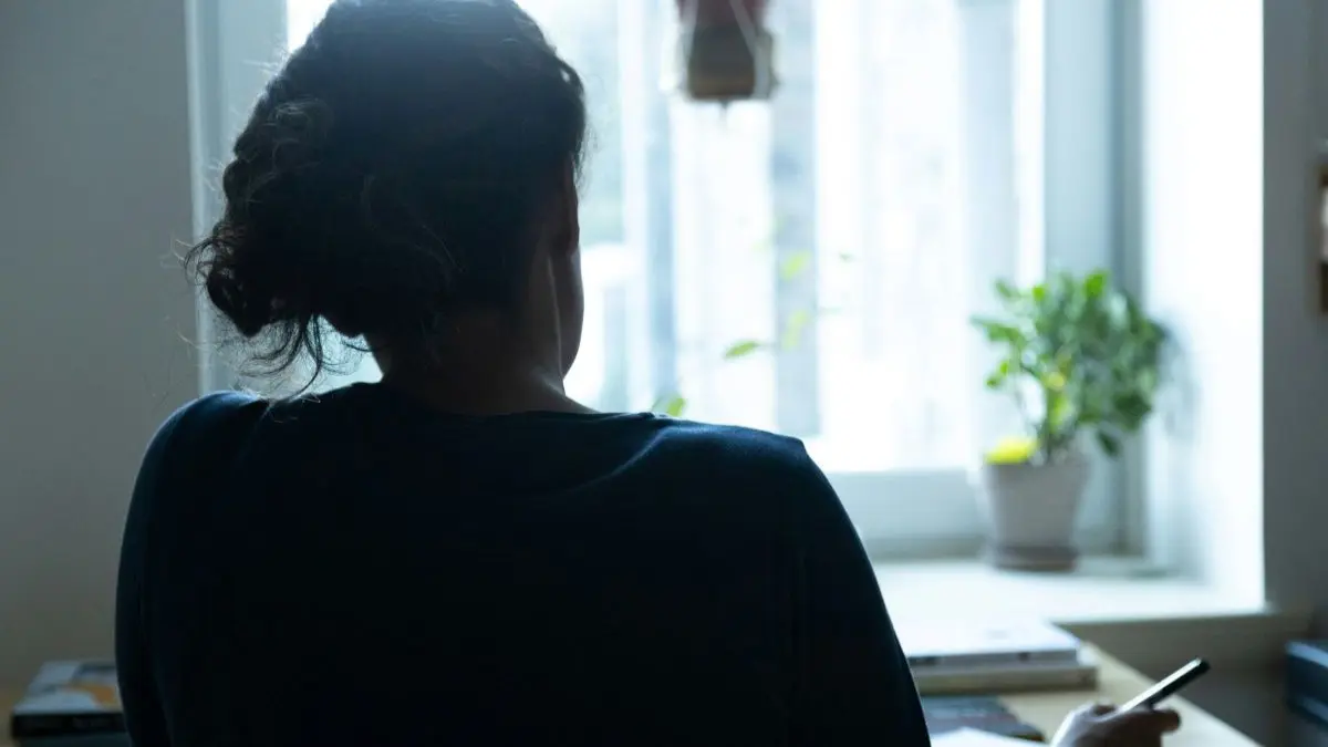 Vrouw kijkt vanuit een donkere ruimte naar het licht buiten.