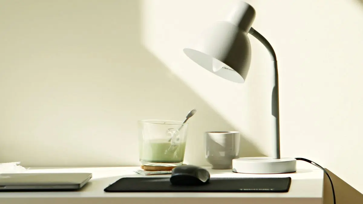 Bright workspace with a desk lamp, laptop, mouse and two cups.