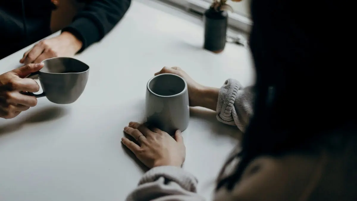 Twee mensen in gesprek aan een tafel, ieder met een mok in de hand.