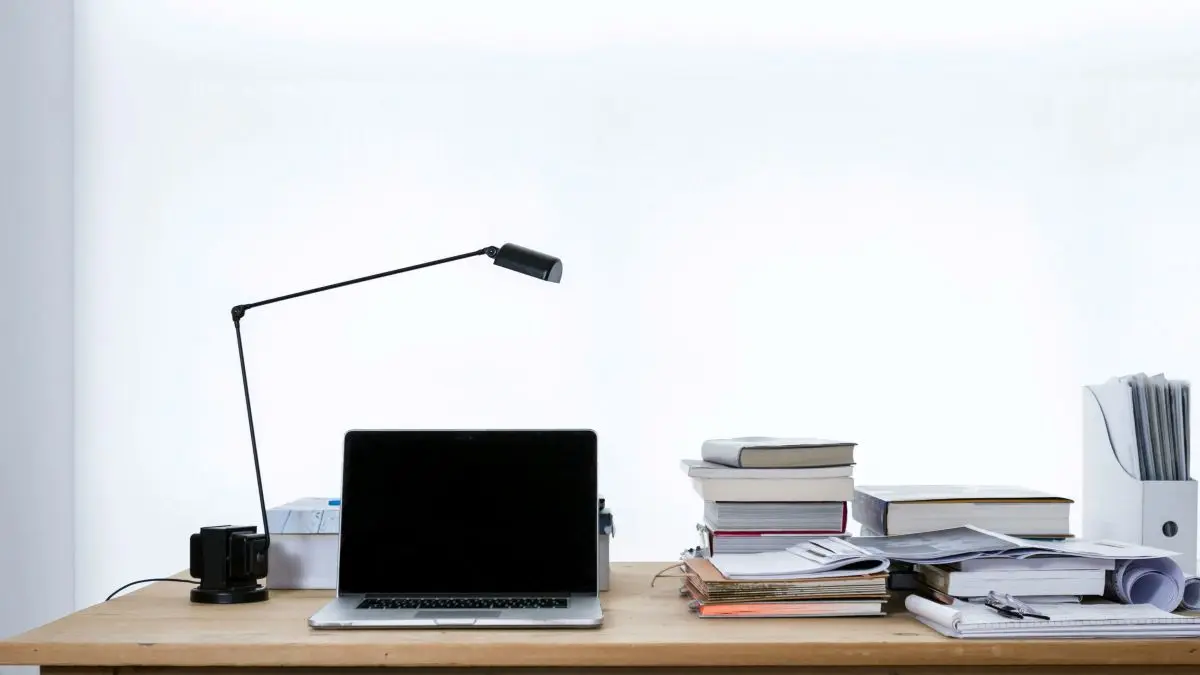Workspace with a laptop, desk lamp, books, documents and journals.