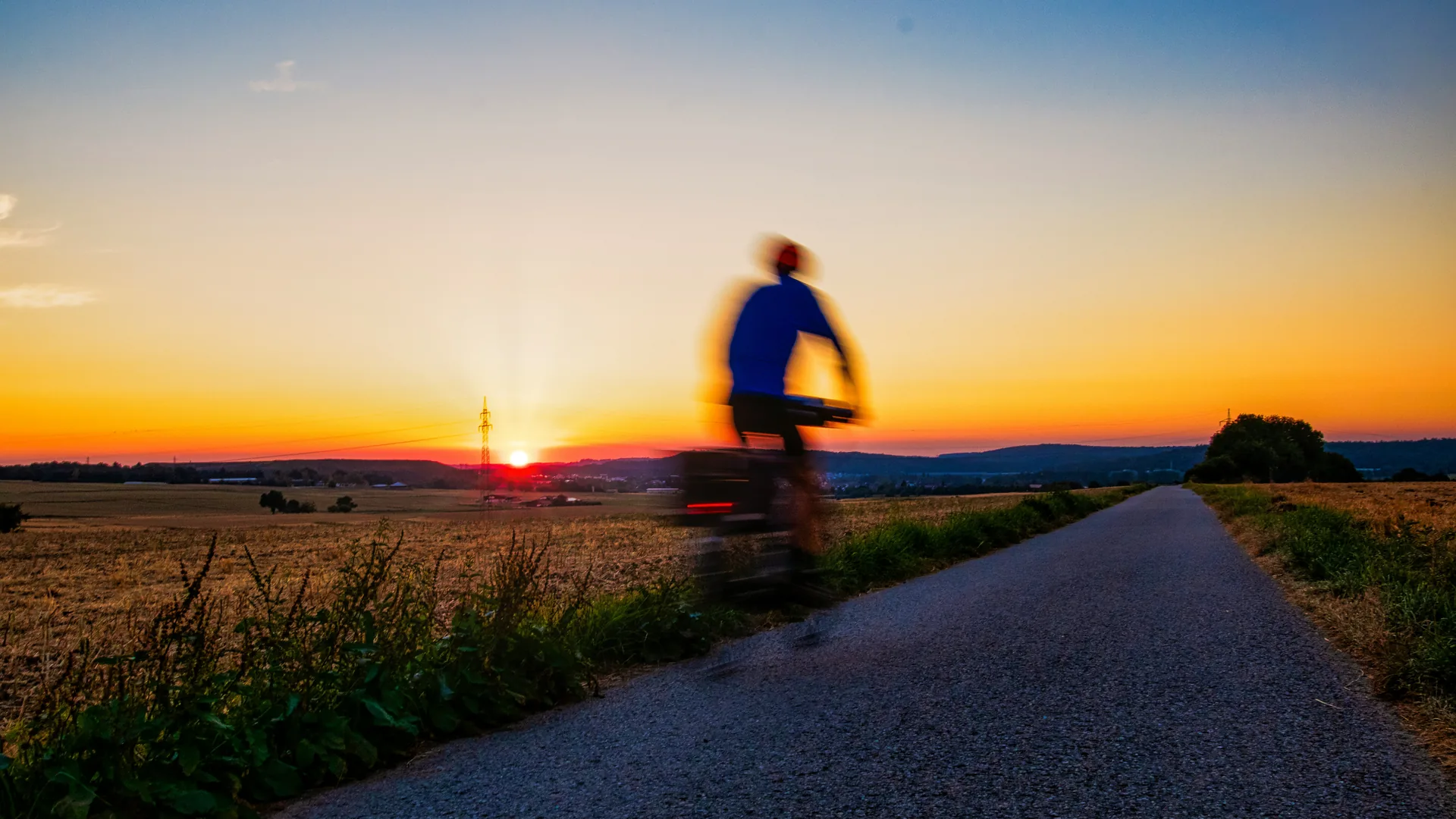 A cyclist in motion rides along a country road at sunset.